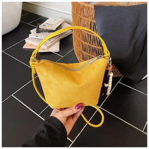 Detalle del bolso tipo cubo de ante amarillo con colgante de madera y cremallera