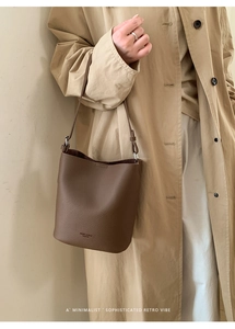 Detail of a brown lychee-patterned bucket bag shown on shoulder with elegant city wear