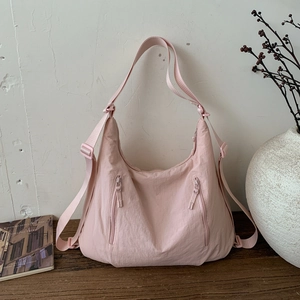 Détail du sac croissant en nylon rose clair avec deux poches zippées sur une table