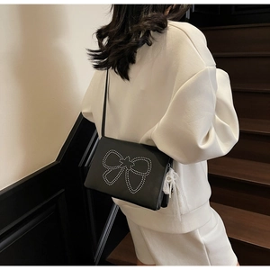 Detail of black crossbody bag with silver rivet bow and white lace pearl pendant charm