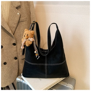 Detail of black crossbody bag with contrast white stitching and cute brown bear charm