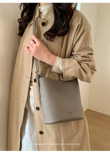 Detailed view of grey pebble leather bucket bag with brand logo and adjustable shoulder strap