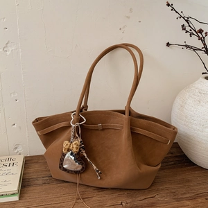 Close-up of caramel brown suede tote bag with leopard print heart charm on wooden table