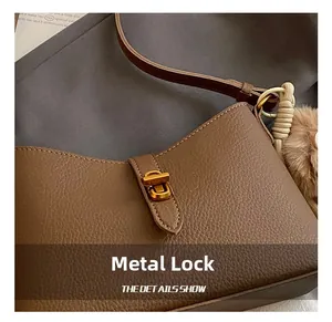 Gros plan du fermoir doré sur sac en cuir marron foncé avec pendentif tissé élégant