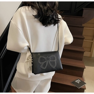Rear view of black square crossbody bag with rivet bow and pearl lace charm on model