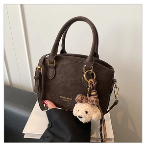 Close-up of matte dark brown handbag featuring gold logo and plush dog charm