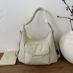 Minimalist beige nylon tote bag with curved front pocket on a rustic wooden table
