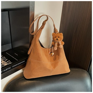 Detail of a brown suede crossbody bag featuring white cross-stitching and a bear charm