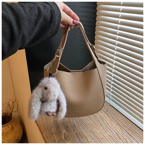 Close-up of khaki lychee leather bucket bag with cute plush bunny charm and silver buckle