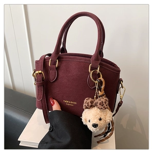 Detail of burgundy crossbody bag with golden hardware and plush bear charm decoration