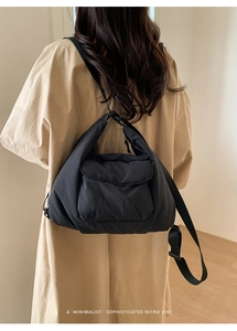 Close-up of black quilted puff shoulder bag with wide adjustable strap on a trench coat