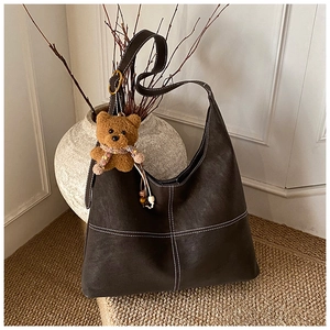 Detail view of a vintage dark brown leather tote bag with white contrast stitching and charm