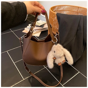 Detail of dark brown leather bucket bag featuring a cute plush bunny charm and strap