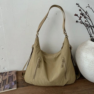 Détail du sac hobo en nylon kaki avec poches zippées sur un support en bois