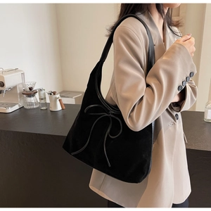 Detail of black matte suede shoulder bag with a large decorative leather bow on the side