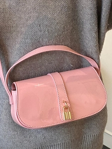 Chic pink patent leather shoulder bag with gold padlock shown on a grey sweater
