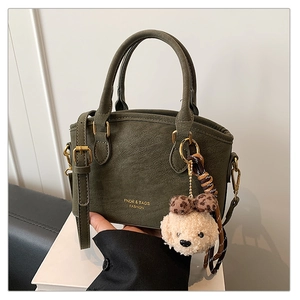 Detail of dark green leather handbag with gold hardware and plush bear charm