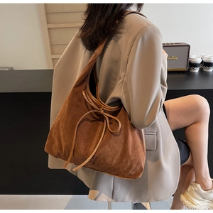 Detail of a brown matte shoulder bag with drawstring bow on a model in a cafe