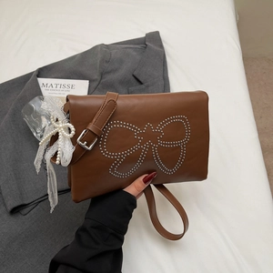 Close-up of brown leather bag with rivet bow pattern and pearl lace charm detail