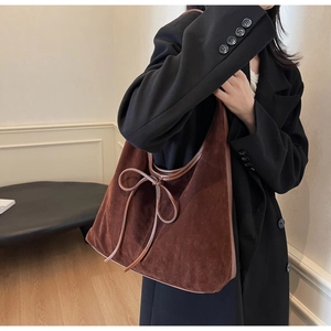 Detail of a large brown suede tote bag featuring a decorative bow tie and retro style