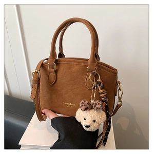 Detail of brown faux leather handbag with gold logo, plush charm, and woven strap accessory