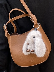 Brown leather hobo bucket bag with a plush bunny charm on a black outfit background