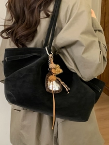 Minimalist black faux suede large tote bag with heart charm and tassel detail on model