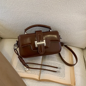 Detail of brown vintage small square bag with silver metal lock on white textured sofa