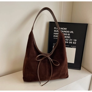 Detail of a dark brown suede hobo bag with an elegant leather bow tie on a white table