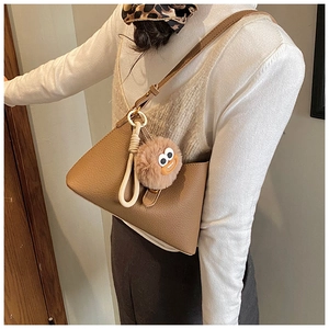Détail du sac marron à motif litchi avec breloque en peluche et accessoire de nœud tissé