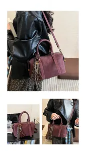 Detail of dark purple Boston bag with matte texture, tassel charm, and shoulder strap