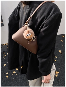 Détail du sac à bandoulière en cuir marron foncé avec charm monstre en peluche sur manteau noir