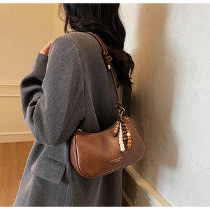 Detail of a brown leather shoulder bag with beaded fringe charm and knotted strap detail