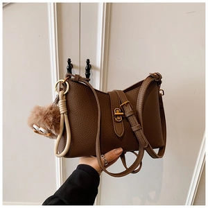 Détail du sac bandoulière en cuir marron avec boucle dorée et breloque en peluche marron