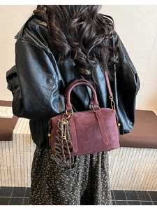 Detail view of burgundy Boston bag with soft suede finish and decorative brand pendant