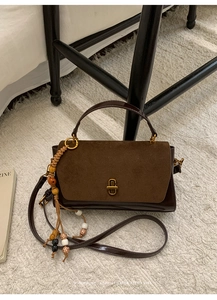 Close-up of vintage brown handbag featuring mixed textures, metal lock, and beaded tassel