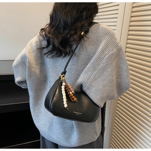 Detail of black faux leather crescent bag with decorative beaded tassels on grey sweater
