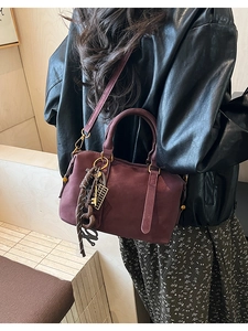 Detail view of Bordeaux red Boston bag with gold hardware and woven charm accessory