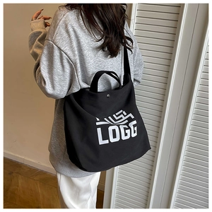 Detail of black canvas tote bag showing LOGG print, snap closure, and crossbody strap