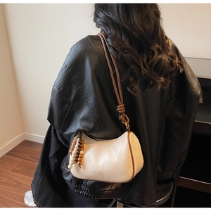 Detail of cream white leather shoulder bag with brown trim and wooden bead accessory