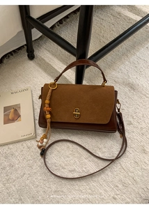 Detail of retro mixed-texture crossbody bag with golden twist lock and beaded charm
