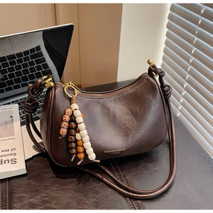 Detail of dark brown crescent bag with top knot strap and wooden bead charm accessory