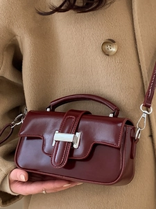 Minimalist burgundy patent leather handbag with silver clasp on a wool coat background
