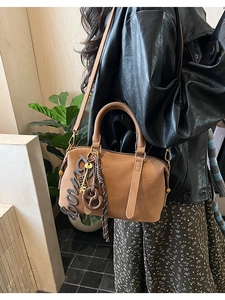 Detailed view of a brown Boston bag with golden hardware and artistic pendant charms