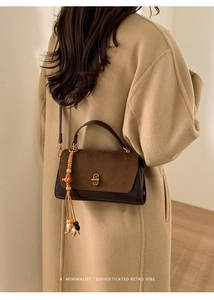 Close-up of retro brown handbag with wooden bead tassel on a beige long coat