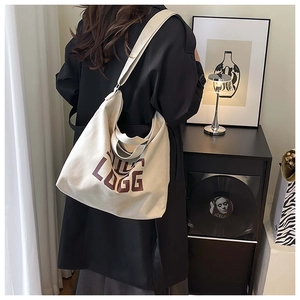 Artistic cream canvas tote bag with brown logo shown in a stylish lifestyle interior setting