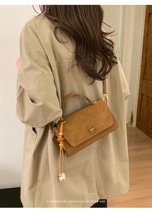 Detailed side view of caramel brown matte handbag featuring retro gold lock and wooden bead tassel