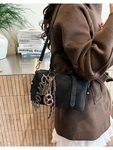 Detail view of black Boston bag with decorative charms and woven tassel details
