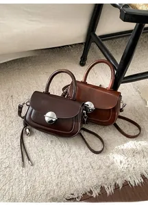 Detail of square crossbody bags in dark brown and reddish brown with silver metal buckles