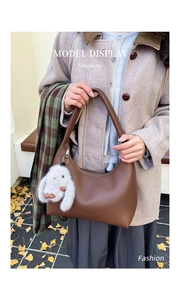Detailed view of a brown leather Hobo bag with a plush rabbit pendant in autumn setting